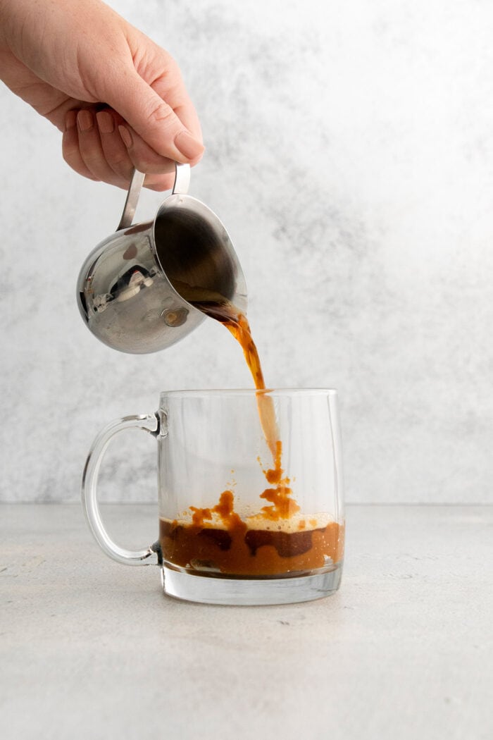 This Pumpkin Spice Latte has a base of pumpkin sauce sweetened with maple sugar that's mixed with strong espresso and topped with frothy milk. Espresso is poured into a glass mug.