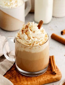 A glass of pumpkin spice latte topped with whipped cream and a cinnamon stick.