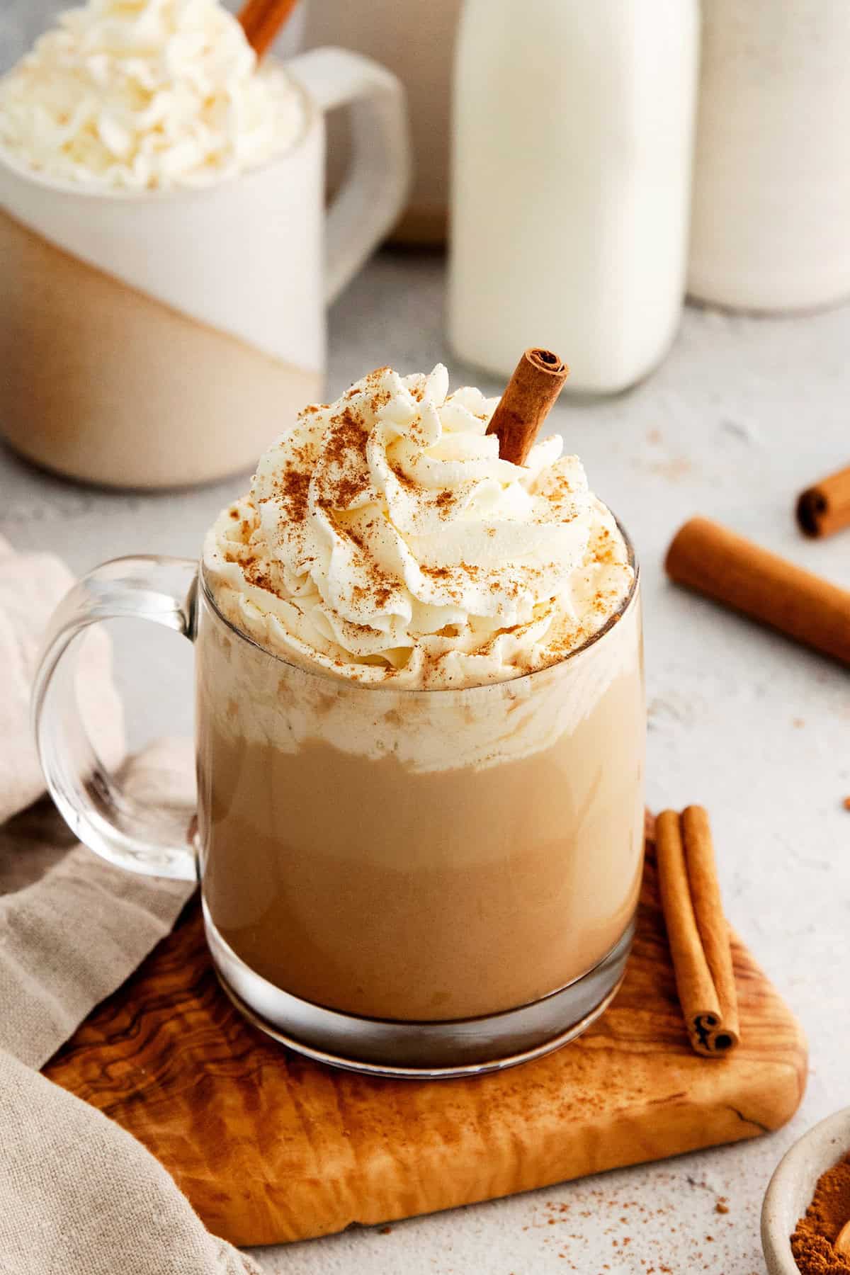 A glass of pumpkin spice latte topped with whipped cream and a cinnamon stick.