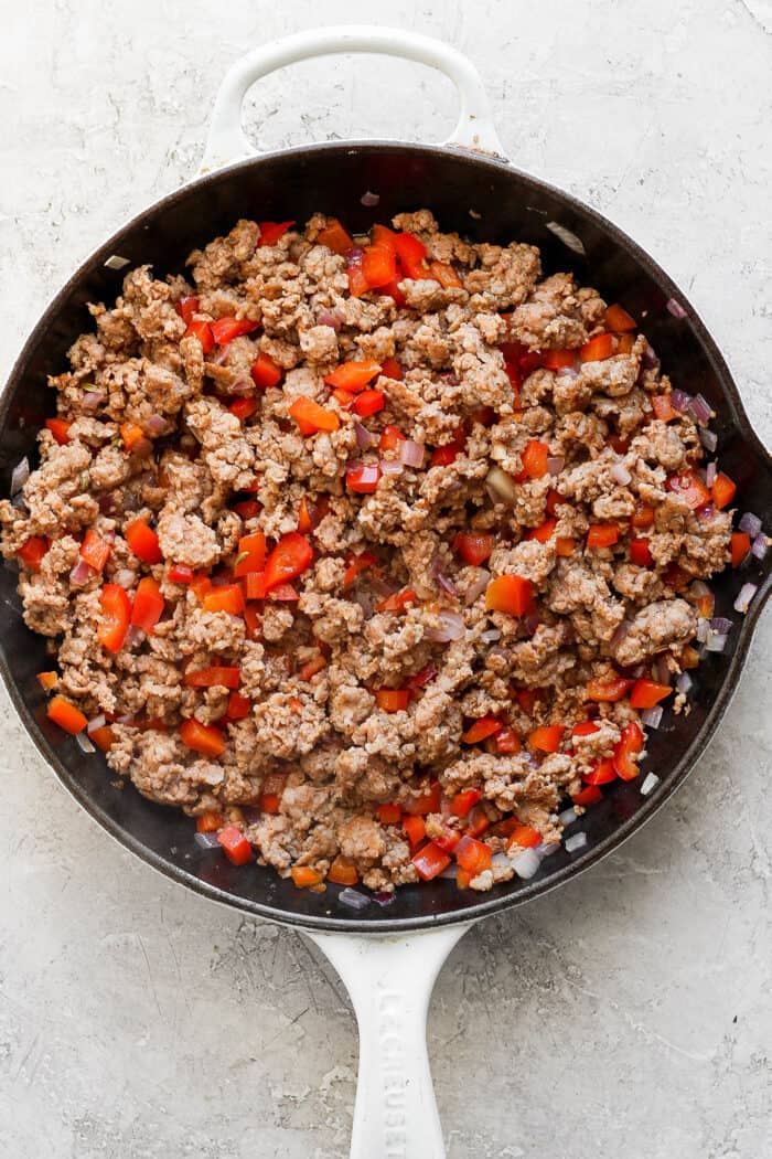 This garlicky tater tot breakfast casserole recipe with red peppers, onions, and sausage is an effortless morning bite. Browned sausage and veggies in the skillet.