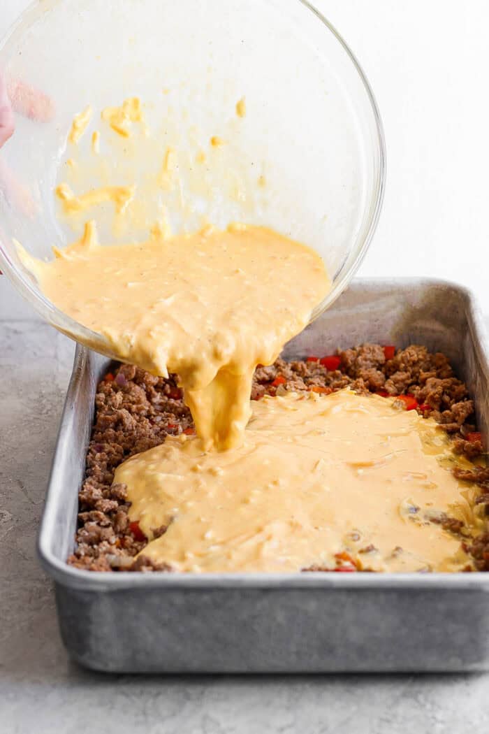 This garlicky tater tot breakfast casserole recipe with red peppers, onions, and sausage is an effortless morning bite. Pouring the egg mixture over the sausage-veggie mixture in the casserole dish.