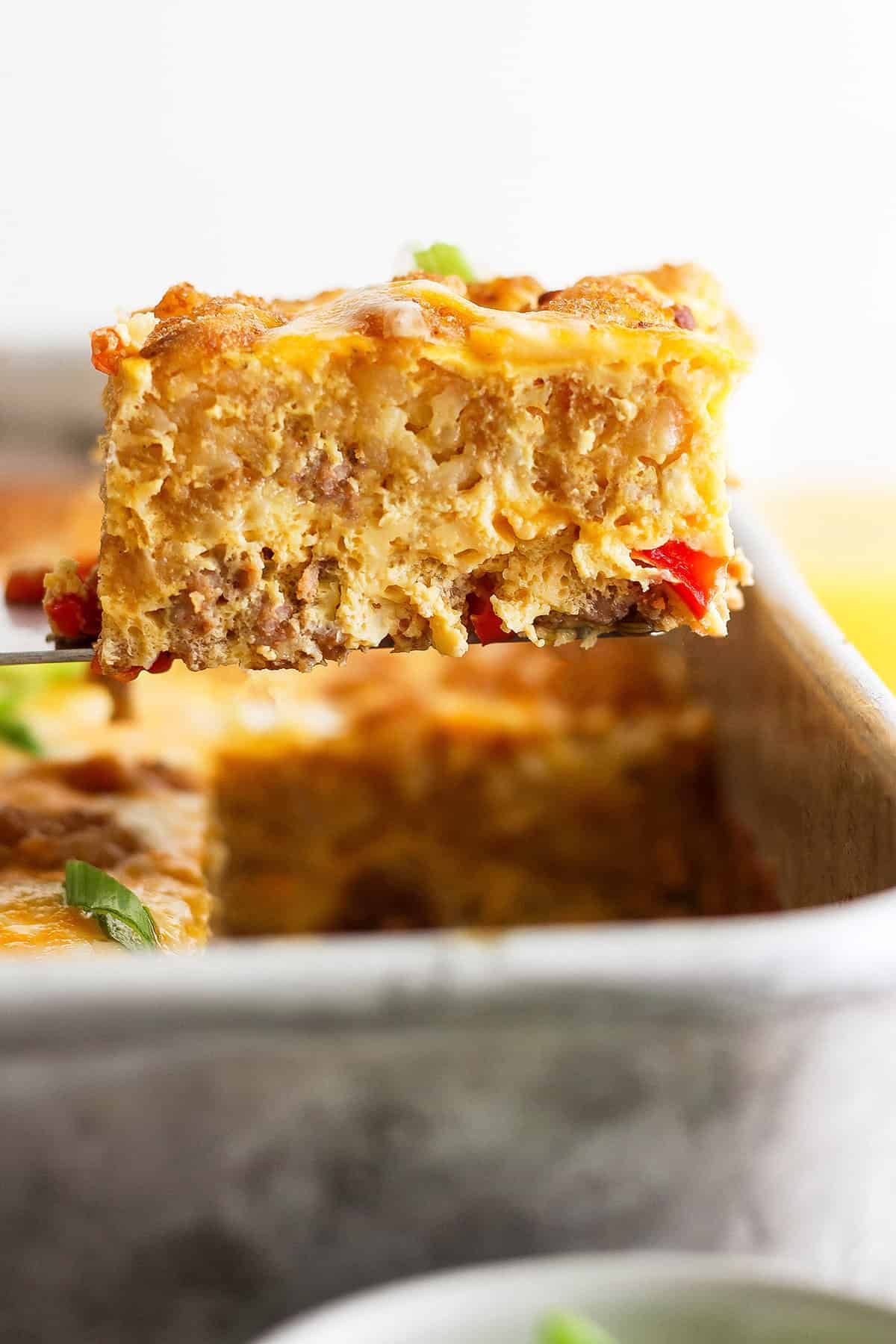 This garlicky tater tot breakfast casserole recipe with red peppers, onions, and sausage is an effortless morning bite. Close-up of a slice of tater tot casserole with eggs, sausage, and veggies.