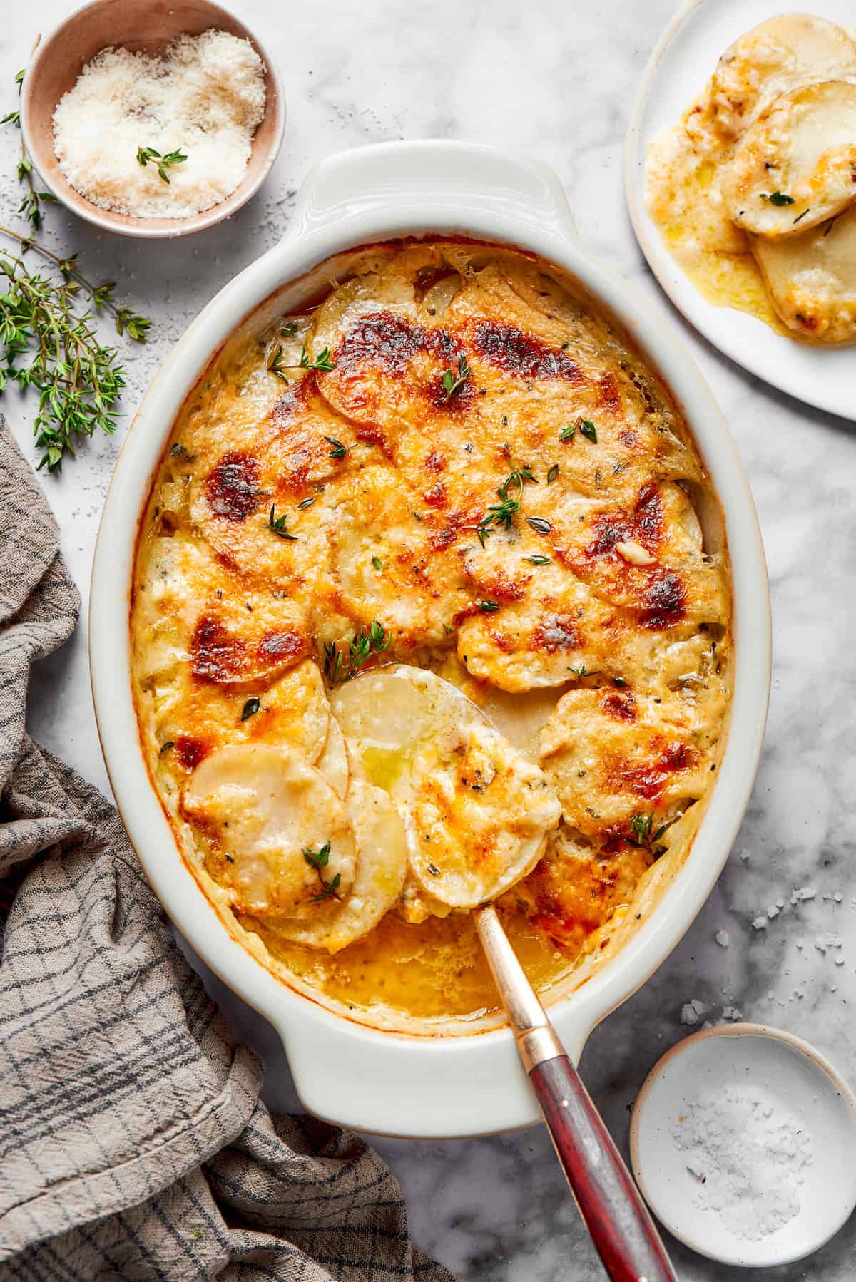 overhead photo of a white oval baking dish with cheesy scalloped potatoes
