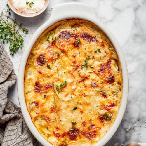 overhead photo of an oval white baking dish of cheesy scalloped potatoes