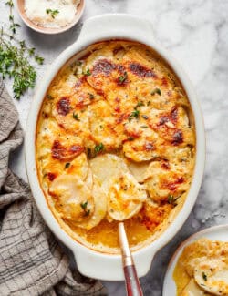 Melty scalloped potatoes garnished with fresh herbs in the baking dish.
