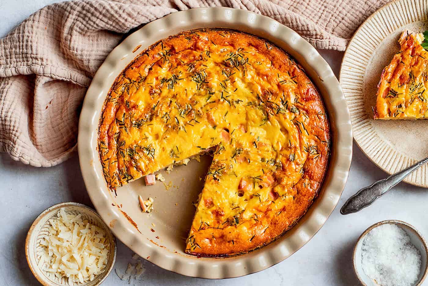 This cheesy crustless quiche recipe with ham, tangy Dijon, and chives is an easy baked dish for the holidays. overhead photo of a pie plate of baked crustless quiche