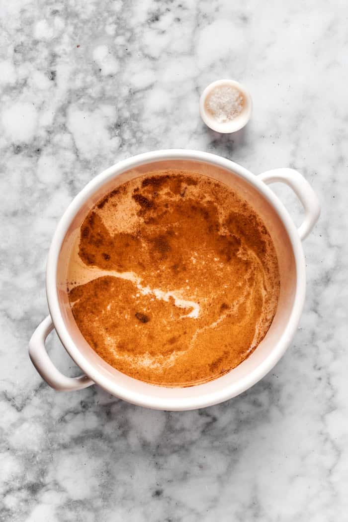 This spiced homemade eggnog recipe with brandy, smokey rum, and fluffy whipped cream is the perfect cocktail for holiday gatherings. heating milk with spices in a white pot