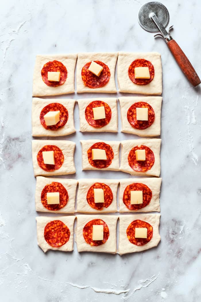 Homemade pizza bites tuck pepperoni and gooey mozzarella into seasoned pizza dough, then they're baked with even more cheese on top. Yum! Squares of pizza dough topped with pepperoni and mozzarella