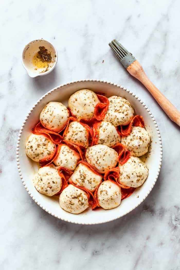 Homemade pizza bites tuck pepperoni and gooey mozzarella into seasoned pizza dough, then they're baked with even more cheese on top. Yum! Pizza bites after brushing with herb oil
