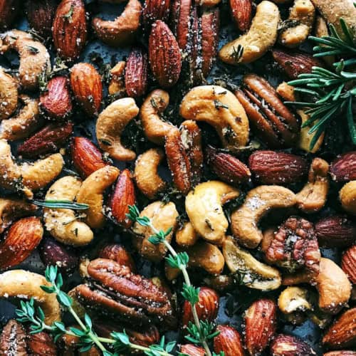 a pan of spiced nuts with fresh rosemary and thyme
