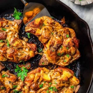 a cast iron skillet with juicy baked pork chops covered in stuffing and gravy