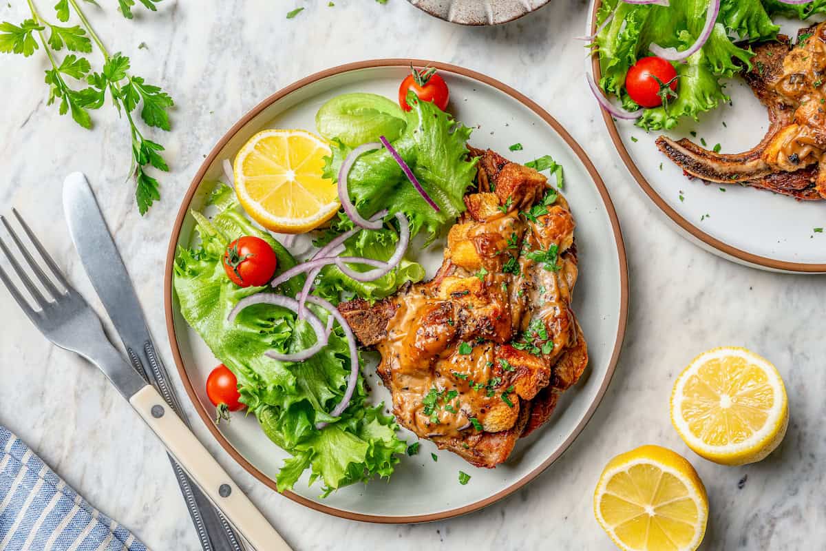a pork chop with stuffing and gravy on a plate with a fresh green salad
