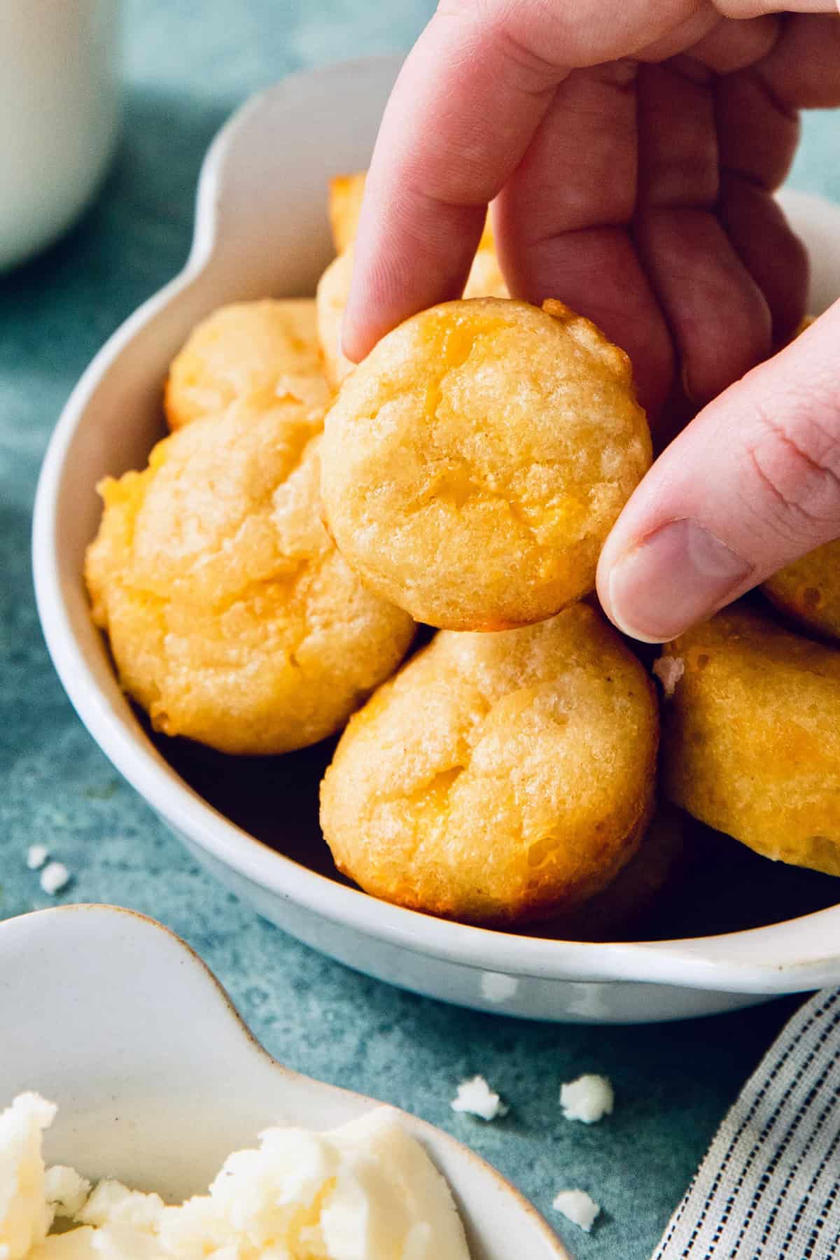 This Colombian Pandebono recipe is fantastically cheesy, surprisingly easy, and irresistibly tender and fluffy. So delicious! Handing picking up pandebono from bowl