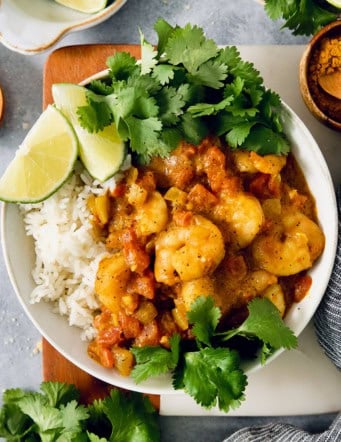 Overhead view of shrimp curry in bowl with rice, cilantro, and lime wedges