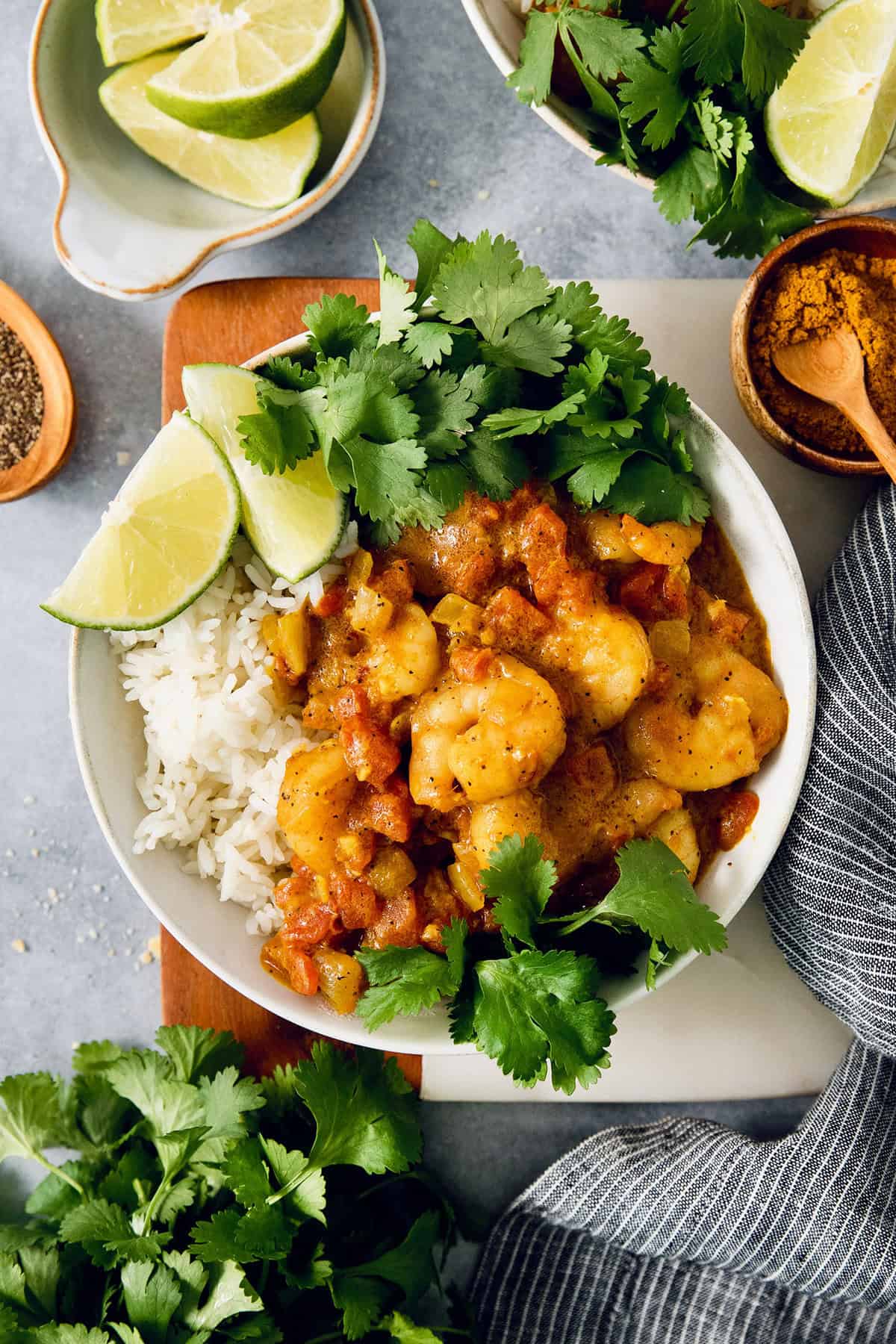 This easy Shrimp Curry recipe combines elements of Thai and Indian curries for a uniquely delicious weeknight meal. So quick and easy! Overhead view of shrimp curry in bowl with rice, cilantro, and lime wedges