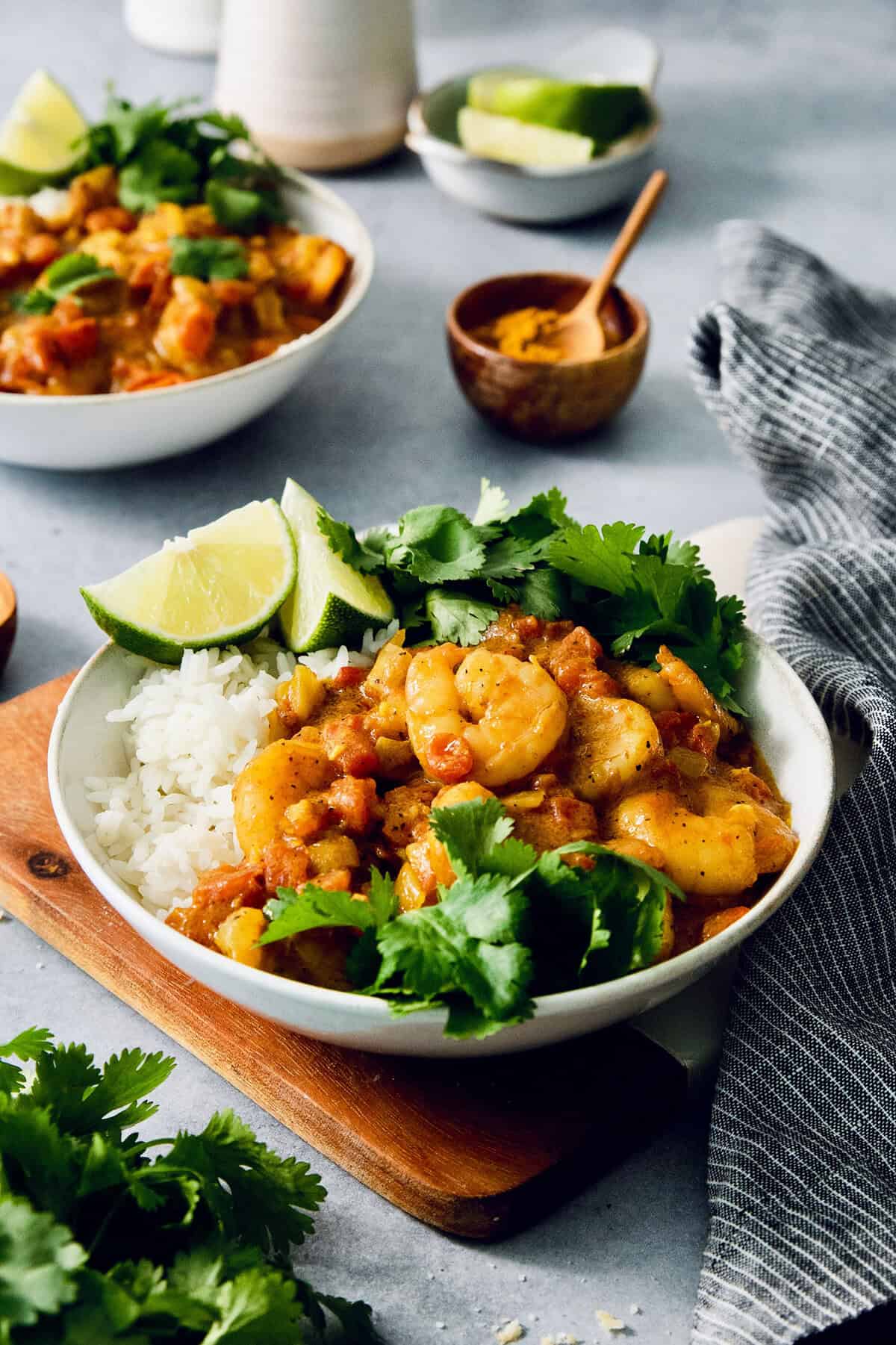 This easy Shrimp Curry recipe combines elements of Thai and Indian curries for a uniquely delicious weeknight meal. So quick and easy! Bowl of shrimp curry with rice, cilantro, and lime wedges