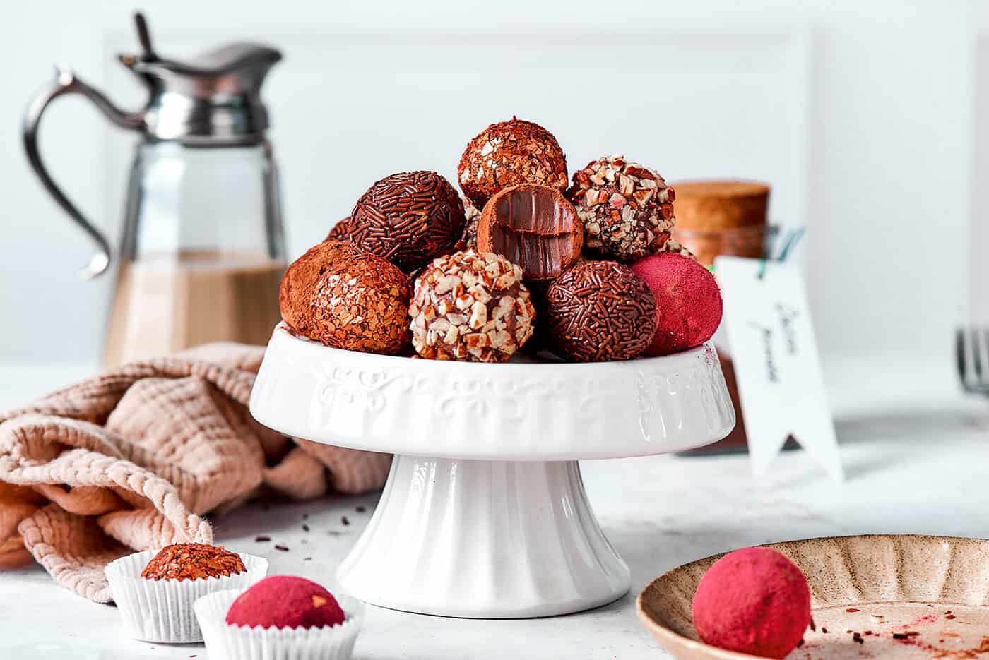 Melt-in-your-mouth Chocolate Truffles are an indulgence worth making from scratch. This easy recipe calls for only 6 simple ingredients! chocolate truffles rolled in a variety of coatings, on a white pedestal platter