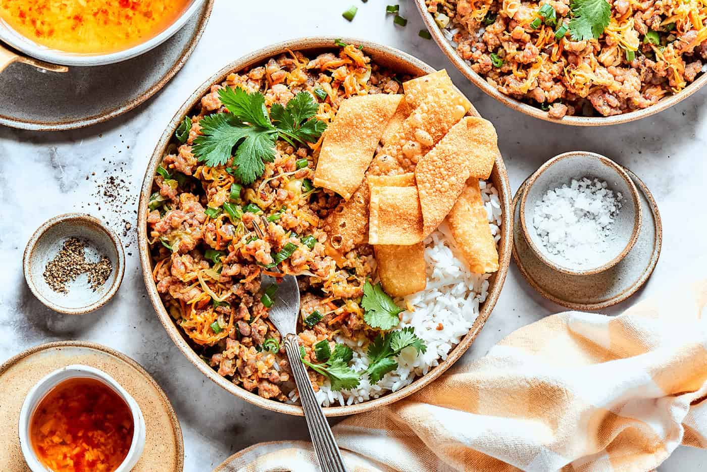 This easy Egg Roll in a Bowl recipe is loaded with ground pork, cabbage and carrots. Served with crispy wonton strips and a tasty Asian sauce! egg roll in a bowl, served in pottery bowls over white rice