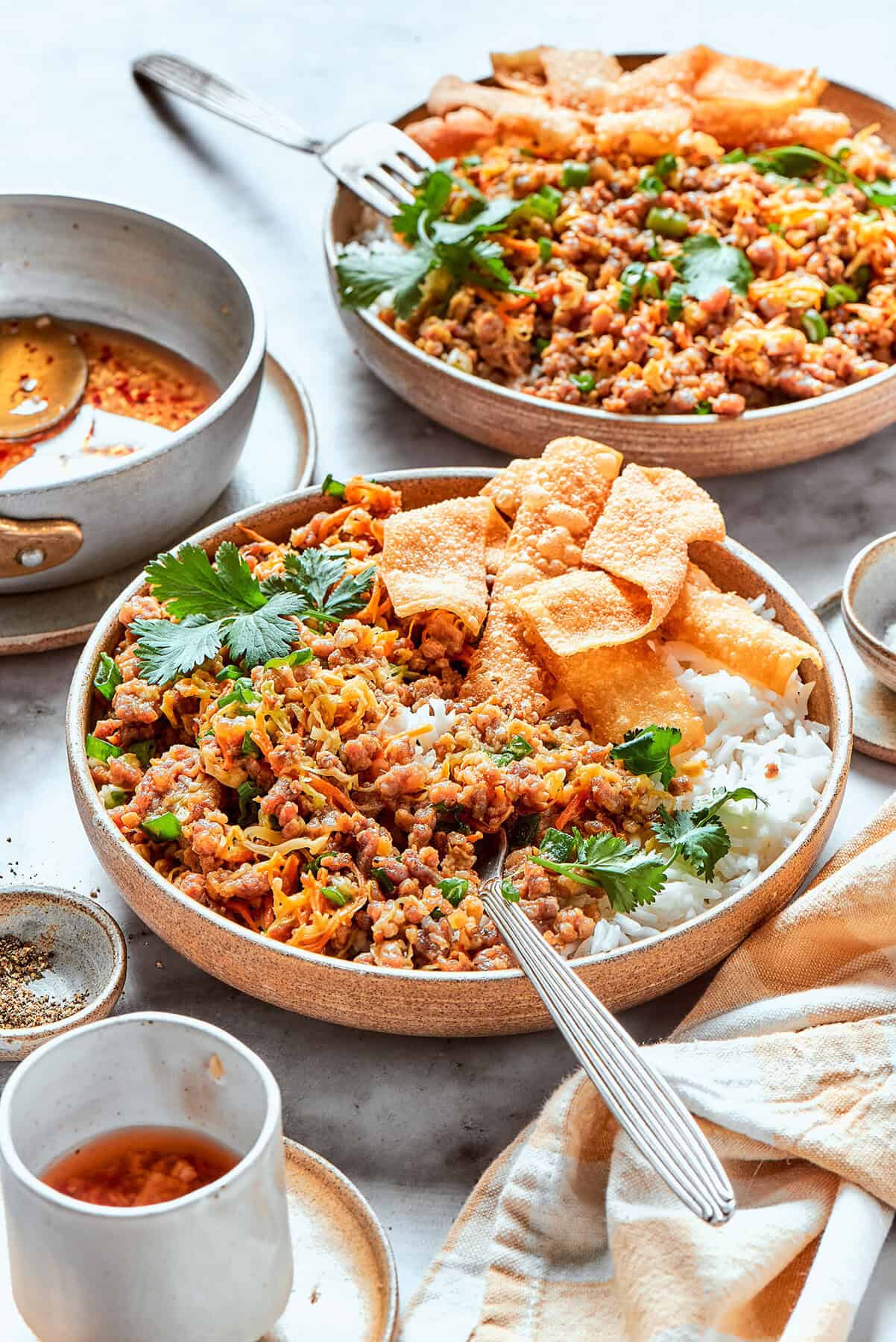 This easy Egg Roll in a Bowl recipe is loaded with ground pork, cabbage and carrots. Served with crispy wonton strips and a tasty Asian sauce! egg roll in a bowl, served in pottery bowls over white rice