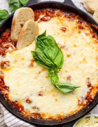 Overhead view of lasagna dip in skillet with two sliced baguette dippers