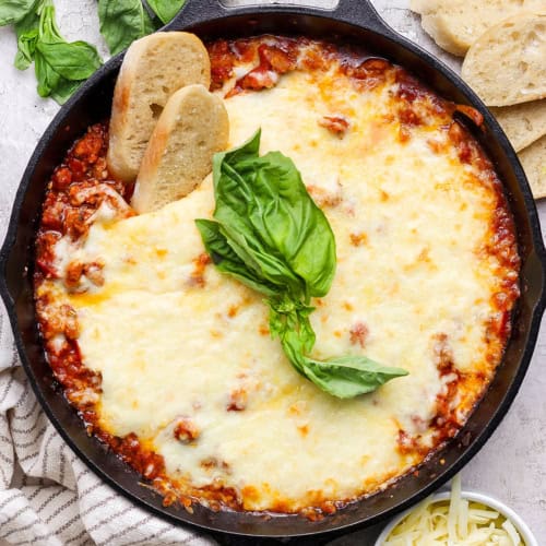Overhead view of lasagna dip in skillet with two sliced baguette dippers