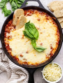 Overhead view of lasagna dip in skillet with two sliced baguette dippers
