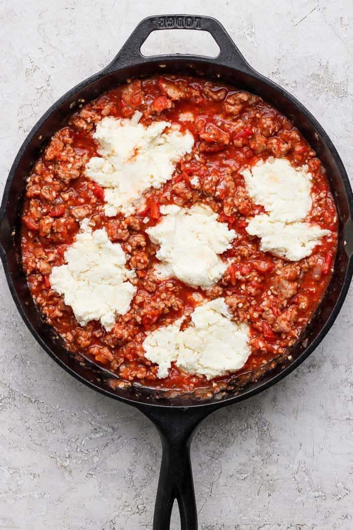 This Lasagna Dip has melty pockets of cheese, meaty sausage, and zesty tomato sauce, all ready for scooping with garlic bread dippers. YUM! Dollops of cheesy yum added to meaty sauce in skillet