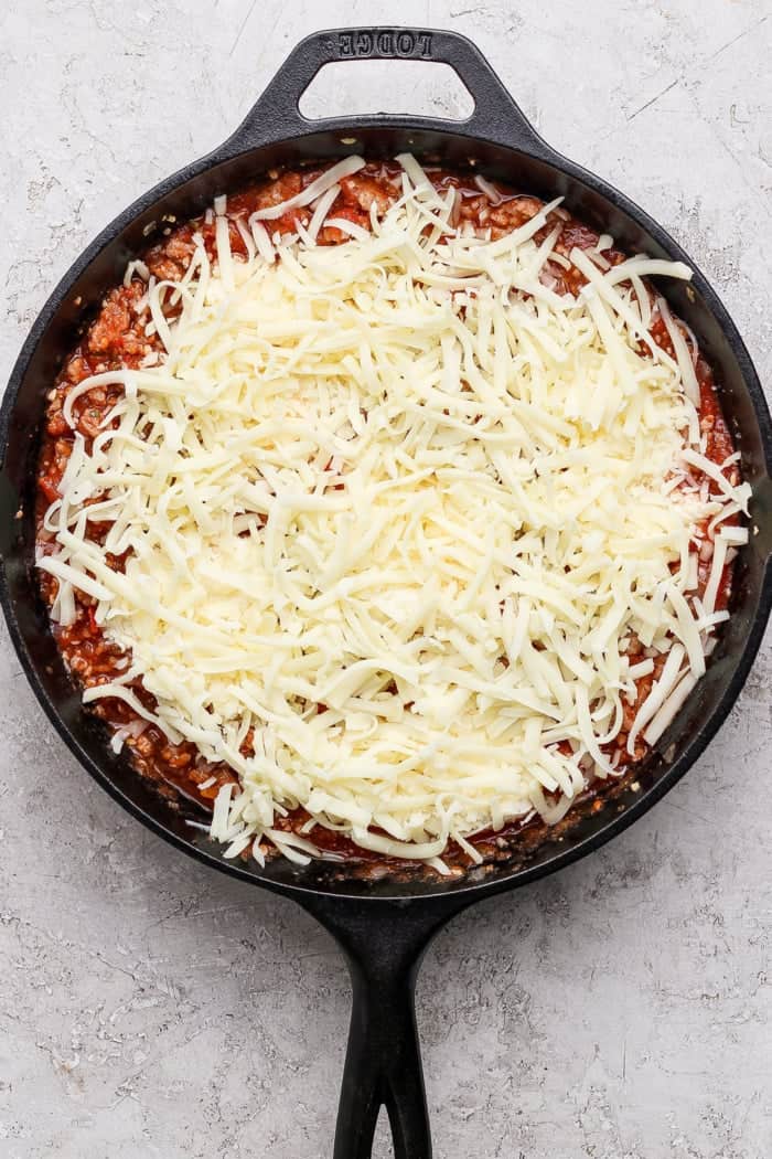 This Lasagna Dip has melty pockets of cheese, meaty sausage, and zesty tomato sauce, all ready for scooping with garlic bread dippers. YUM! Mozzarella added to lasagna dip in skillet