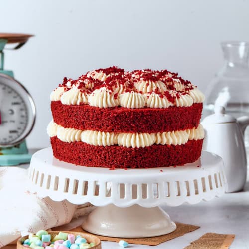 a double layer red velvet cake with cream cheese frosting on a white pedestal
