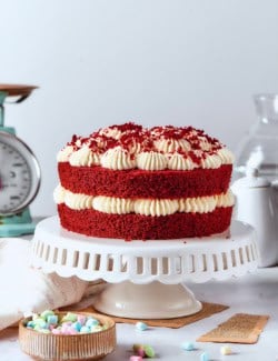 a double layer red velvet cake with cream cheese frosting on a white pedestal