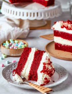a piece of double layer red velvet cake with cream cheese frosting, on a plate