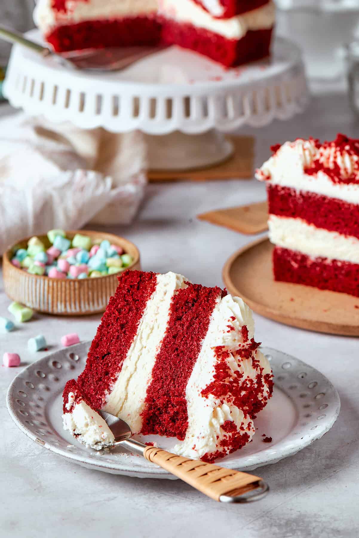 a piece of double layer red velvet cake with cream cheese frosting, on a plate
