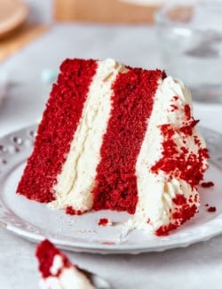 close-up photo of a piece of double layer red velvet cake with cream cheese frosting, on a plate