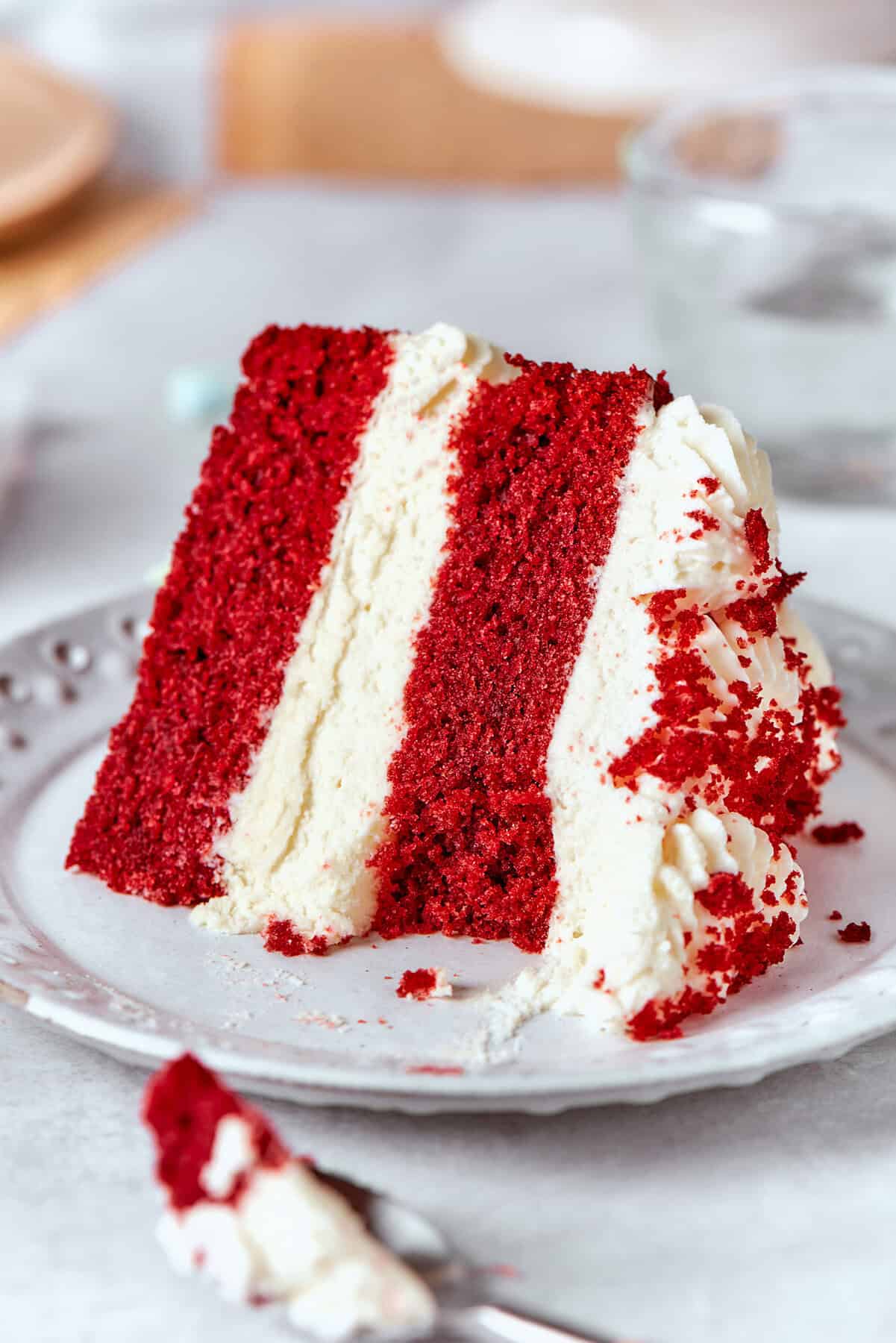 close-up photo of a piece of double layer red velvet cake with cream cheese frosting, on a plate