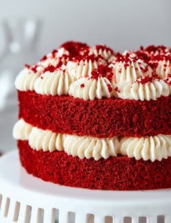a double layer red velvet cake with cream cheese frosting, on a white pedestal
