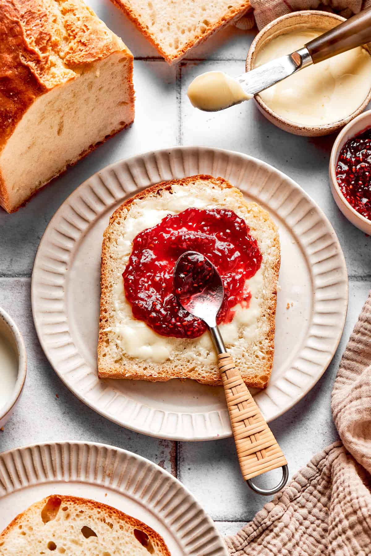 This homemade English Muffin Bread is incredibly easy, with no kneading required, and it will make your morning toast extra delicious! Overhead view of English muffin bread slice on plate with butter and jam