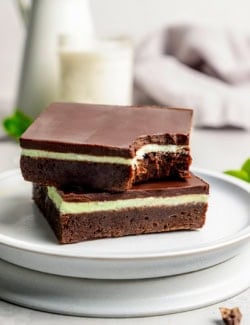 two layered chocolate mint brownies on a plate, one with a bite out of it