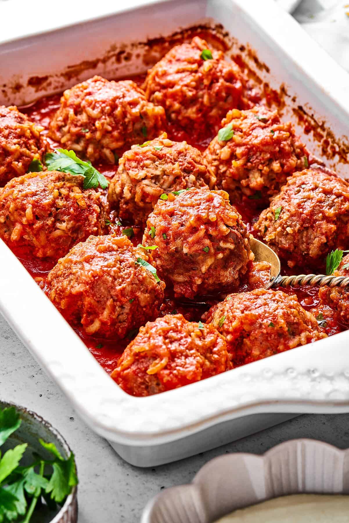 Tender beef and rice Porcupine Meatballs are smothered in tomato sauce to make a savory, filling dish that's perfect with mashed potatoes. a white baking dish of porcupine meatballs in red sauce