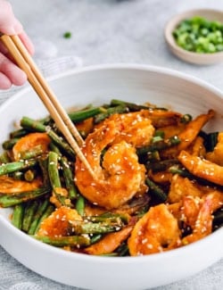 Chopsticks picking up Hunan shrimp from bowl