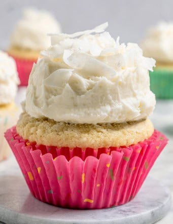 A coconut cupcake with a mound of fluffy coconut frosting, in a pink cupcake liner