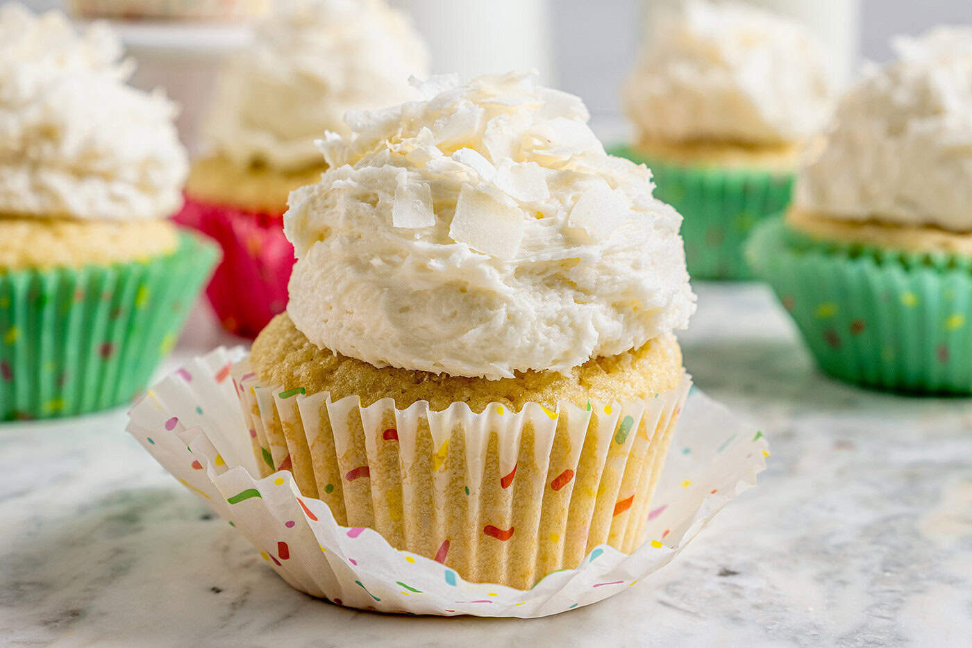 These coconut cupcakes are moist and full of coconut flavor — and just wait until you sink your teeth into the coconut buttercream frosting! coconut cupcakes with coconut frosting, in pastel cupcake liners