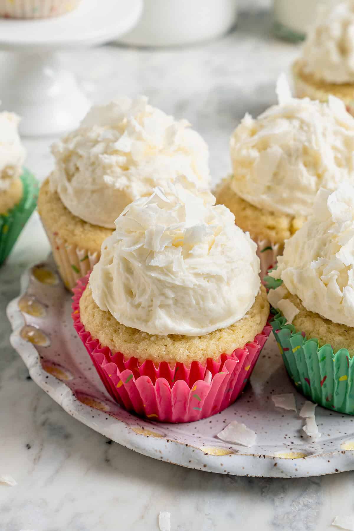 These coconut cupcakes are moist and full of coconut flavor — and just wait until you sink your teeth into the coconut buttercream frosting! coconut cupcakes with mounds of fluffy coconut frosting, in pastel cupcake liners
