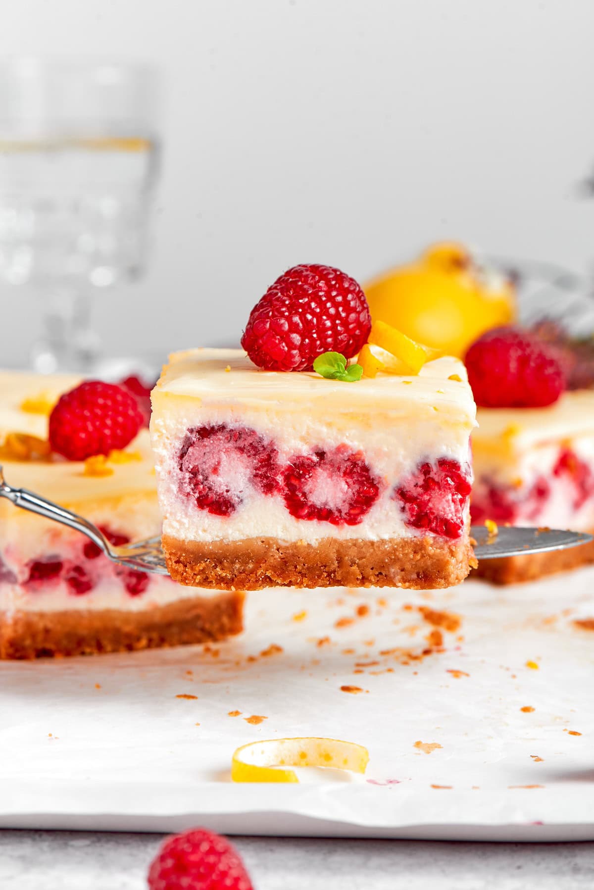 These Lemon Cheesecake Bars with Raspberries are quick to put together, and their lighter texture is perfect for summer. a serving spatula holding a lemon raspberry cheesecake bar