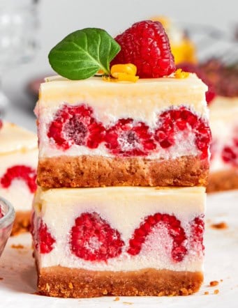 two lemon cheesecake bars with fresh raspberries, stacked on top of each other