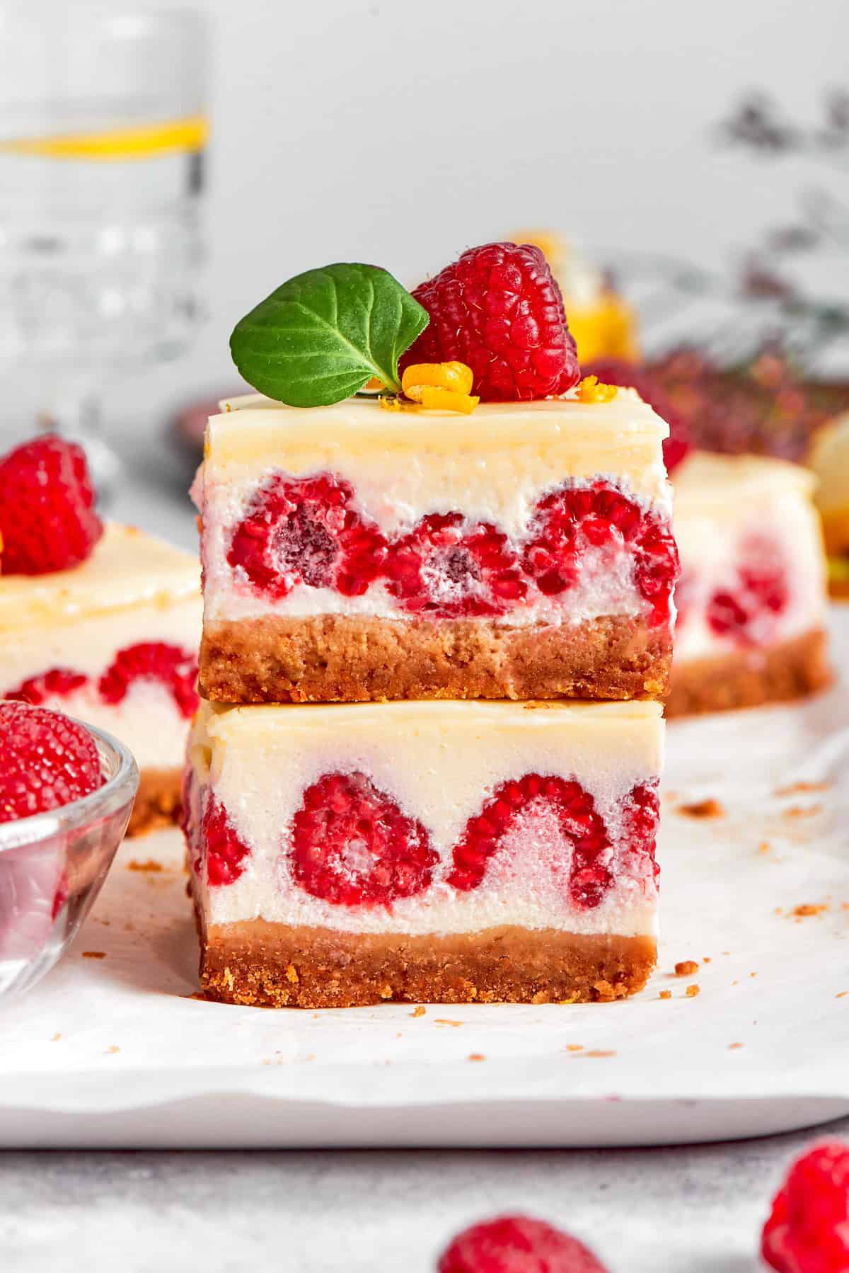 These Lemon Cheesecake Bars with Raspberries are quick to put together, and their lighter texture is perfect for summer. two lemon cheesecake bars with fresh raspberries, stacked on top of each other