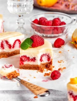 a lemon cheesecake bar with fresh raspberries, with a forkful removed