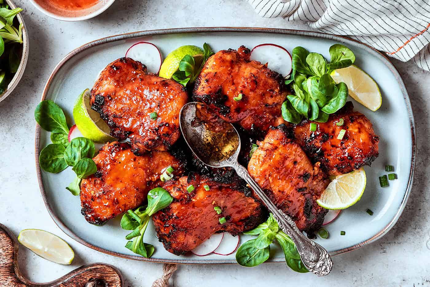 lemongrass chicken thighs on a platter with lime wedges and fresh greens