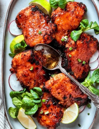 lemongrass chicken thighs on a platter with lime wedges and fresh greens
