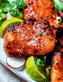 lemongrass chicken thighs on a platter with lime wedges and fresh greens