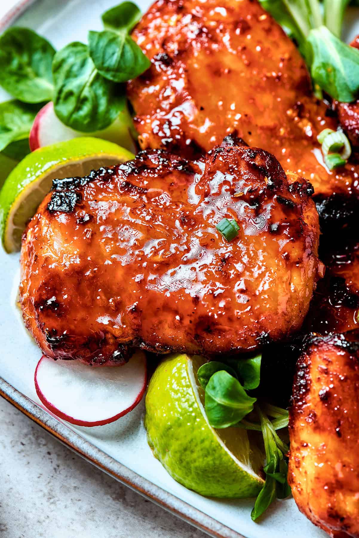 lemongrass chicken thighs on a platter with lime wedges and fresh greens
